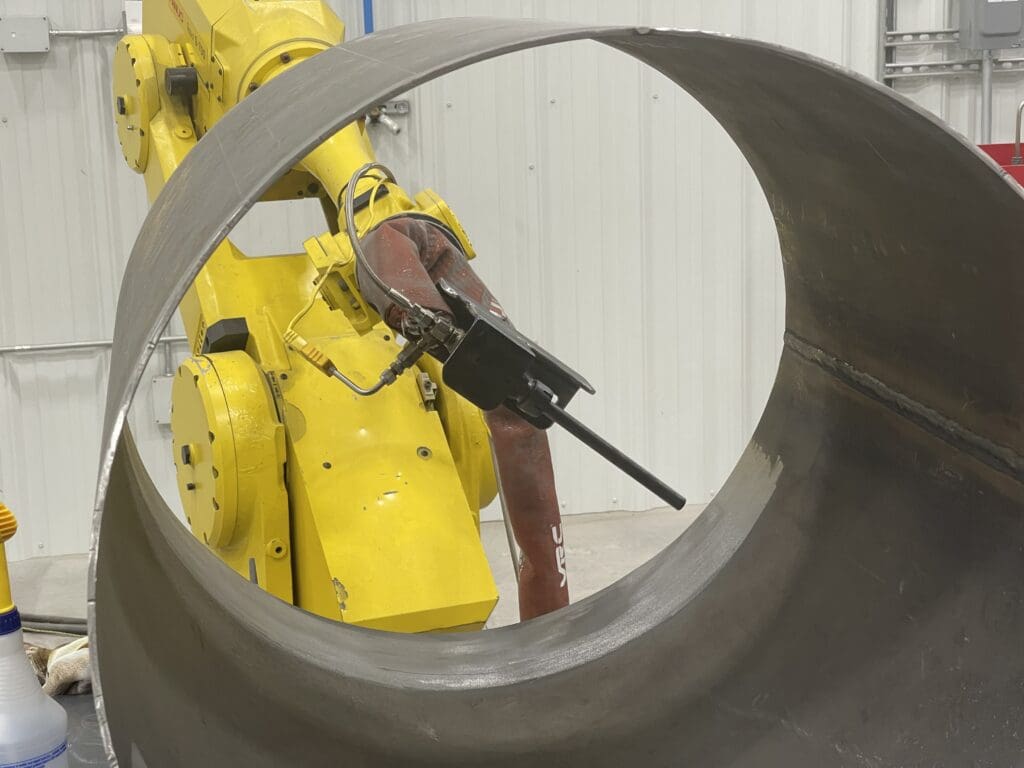robotic arm with cold spray nozzle applying cold spray to a pipe